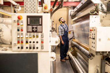 İş kıyafeti ve koruyucu kulaklıklarda işleme hatlarından birine bakan genç üretim kontrol mühendisi