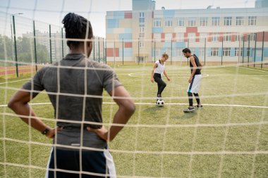 Genç Afrikalı sporcunun arka dansı net duruyor ve sahada futbol topu ile iki oyuncu bakıyor