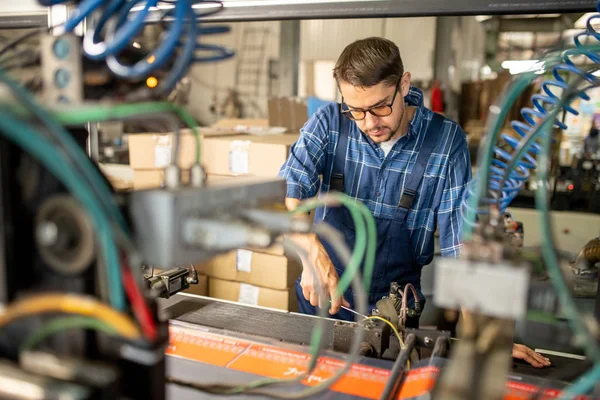 Young repairman or technician serving broken industrial machine or equipment at factory