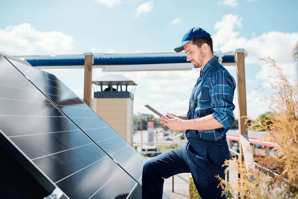 Young master with tablet searching for online data about solar panels installation while standing on rooftop