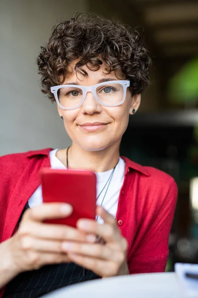 Kafede Akıllı Telefon Kaydırma Sırasında Gözlük Genç Kıvırcık Esmer Kadın — Stok fotoğraf