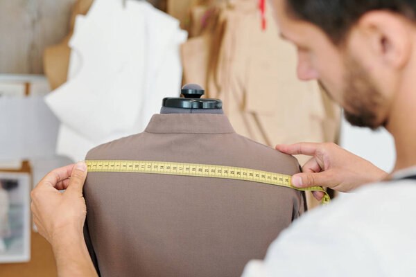 Мужской портной измеряет назад новую куртку на манекен во время работы над незаконченным порядке клиента
