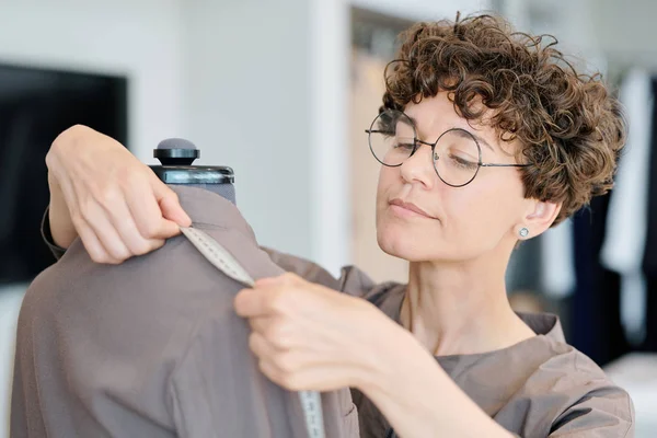 年轻女性裁缝测量未完成夹克的肩长在车间的人体模型 — 图库照片