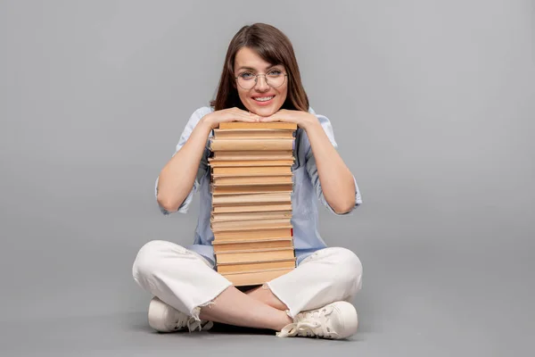 年轻的微笑女学生与她的下巴在高高的书籍堆 阅读看着你孤立 — 图库照片
