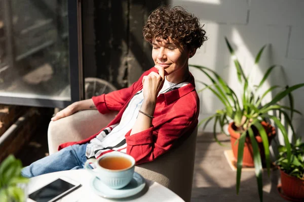 Kafede bitki çay fincanı ile masaönünde koltukta dinlenme zevk zarif casualwear genç gülümseyen kadın