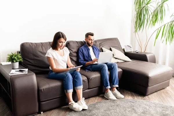 Pareja Joven Concentrada Ropa Casual Sentada Cómodo Sofá Usando Dispositivos —  Fotos de Stock