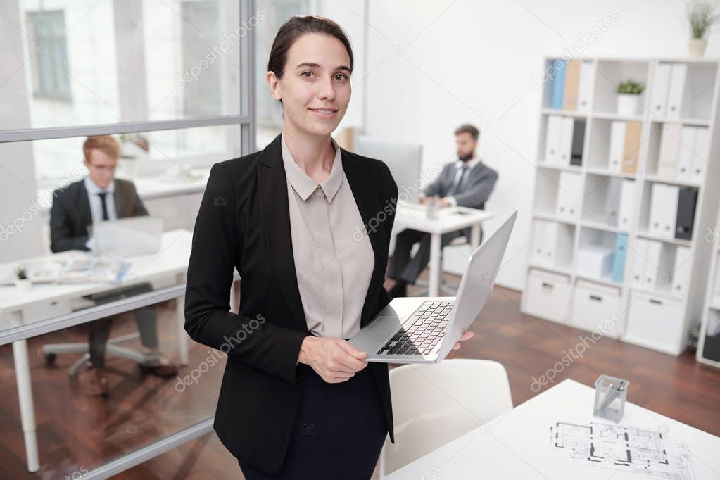 Portrait of elegant young businesswoman standing in office and looking at camera, copy space