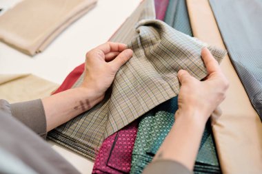 Örneklere bakarken kumaş parçasını tutan ve dikiş elbisesi için uygun olanı seçen insan elleri