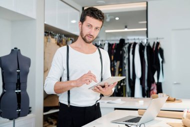 Koleksiyon için yeni modeller için net gezinirken dokunmatik yüzeyli genç yaratıcı moda tasarımcısı size bakıyor