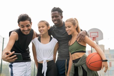 Oyun alanında oyun dan sonra selfie yaparken akıllı telefon kamerasına bakarak aktif giyimli genç sevecen sportif arkadaşlar