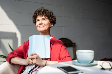 Kafede dinlenirken açık kitap veya dizüstü bilgisayar ile Güzel genç sakin kadın güneşli günde ilham alma
