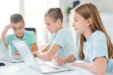 Genç ciddi kız öğrenci ve sınıf arkadaşları masa başında otururken dizüstü bilgisayarların önünde tek tek çalışıyor