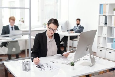 Ofiste, muhasebeci veya yönetici konseptinde çalışırken gözlük takan genç iş kadınının not alma portresi