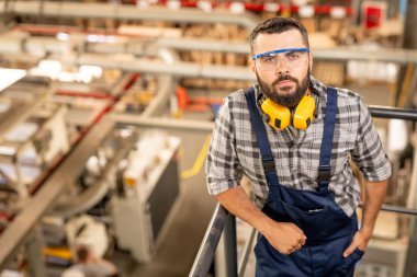 Koruyucu gözlük ve kulaklık size bakarak büyük fabrika genç ciddi teknisyen