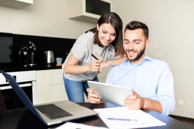 Mutfakta birlikte internet mağazasında mal seçerken dijital tablet kullanarak Pozitif heyecanlı genç çift