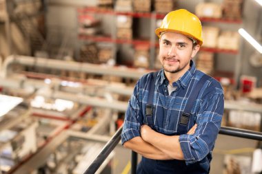 Hardhat ve üniformalı genç başarılı mühendis kamera önünde dururken göğüs tarafından kollarını geçerken