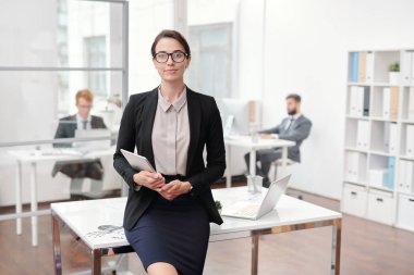 Ofiste poz veren gözlük takan zarif iş kadınının masaya yaslanmış portresi, kopya alanı