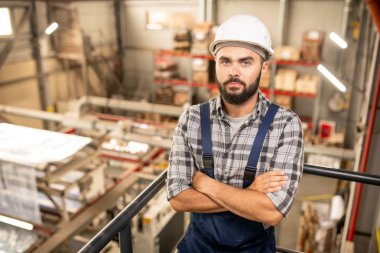 Büyük fabrikanın deposunda dururken tulum ve hardhat göğüs tarafından silah geçiş genç sakallı foreman
