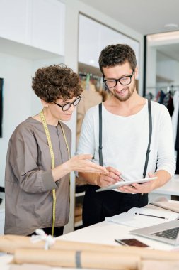 Stüdyolarında yeni koleksiyon üzerinde çalışırken touchpad ekrana işaret eden iki genç yaratıcı tasarımcı