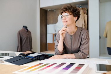 Mutlu genç kadın yaratıcı tasarımcı işyeri tarafından yeni koleksiyon üzerinde çalışırken fikirlerin düşünme