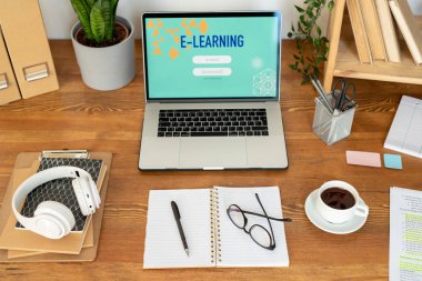 Masadaki iş malzemeleri - dizüstü bilgisayar, bir fincan kahve, açık dizüstü bilgisayar, not defteri yığını nda kulaklıklar