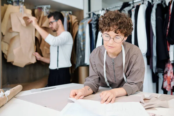 年轻自信的时装设计师在工作期间看着纸上的素描 同时按工作场所处理新模特 — 图库照片