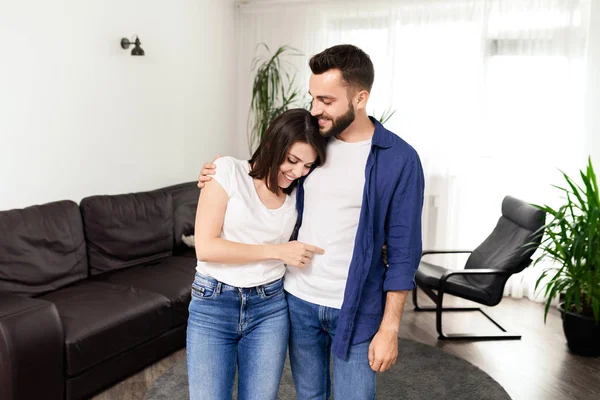 Rahat kıyafetler içinde mutlu heyecanlı genç çift kendi daire oturma odasında ayakta ve hassasiyet ile sarılma