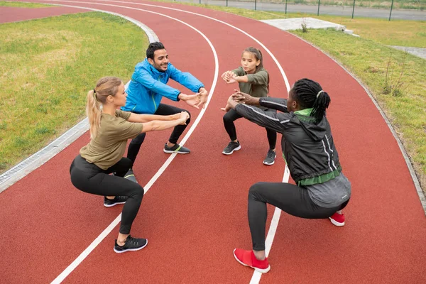Young Intercultural Friends Sportswear Stretching Arms Forwards While Doing Squats — Stock Photo, Image