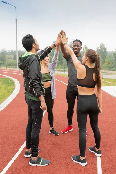 屋外スタジアムで円を描きながら手で触れるスポーツウェアの若い異文化の友人 — ストック写真