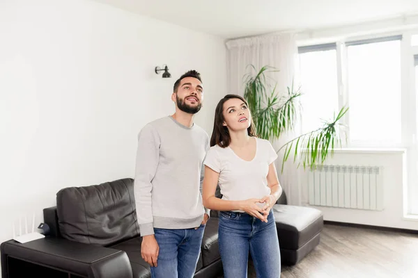 Sonriente Pareja Joven Curiosa Trajes Casuales Pie Habitación Con Muebles — Foto de Stock