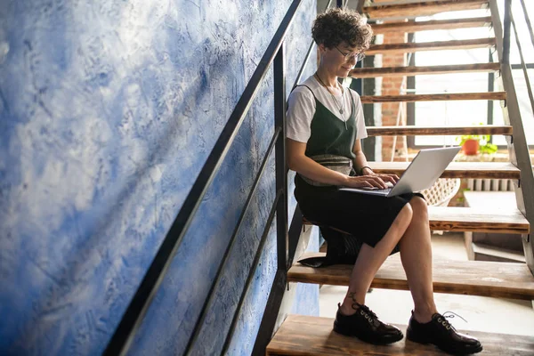 Pretty genç mobil öğrenci veya çalışan dizlerinin üzerinde dizüstü bilgisayar ile merdiven üzerinde oturan ve net çalışan