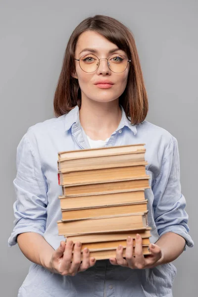 Young serious teacher of literature holding stack of books while carrying them for lesson