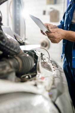 Çağdaş teknik onarım servisinin olgun efendisi tarafından açık makine motoru üzerinde tutulan dijital tablet