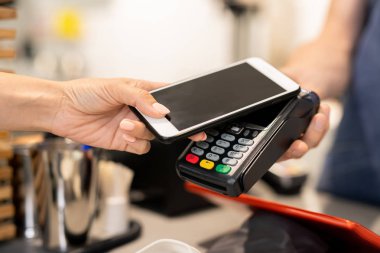 Genç bir kadın cep telefonunu kontak kurmak için kullanıyor. Barista tarafından tutulan elektronik makinenin üzerinde tutuyor.