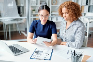 İki genç kadın analist ya da finansör konferans ya da seminer için hazırlanırken masada oturuyorlar.