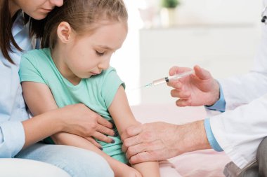 Şirin küçük kız klinikteki doktorun elindeki şırıngaya bakarken iğne olmaktan korkuyor.
