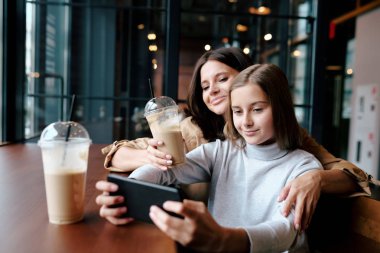 Mutlu bir anne, kafeteryada içki içerken tatlı kızını akıllı telefonuyla kucaklıyor.