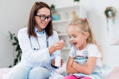 Hasta küçük kız, Whitecoat 'ta hastaneye giderken genç bayan doktorun kaşığından ilaç alıyor.