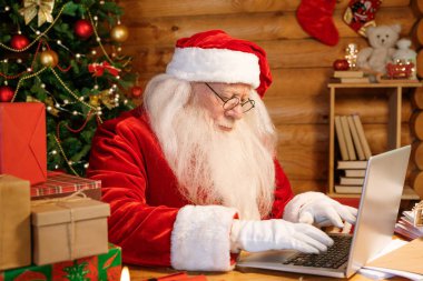 Ciddi bir Noel Baba dizüstü bilgisayarın tuş takımında masa başında yazarken elektronik mektupları cevaplamaya konsantre oluyor.