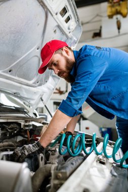 Ciddi genç sakallı makine bakım servisi mühendisi iş sırasında büyük aracın motorunun üzerine eğiliyor.