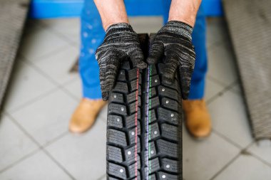 Çağdaş teknik servis elemanının eldivenli elleri lastiği değiştirirken yeni lastikleri ileri taşıyor.