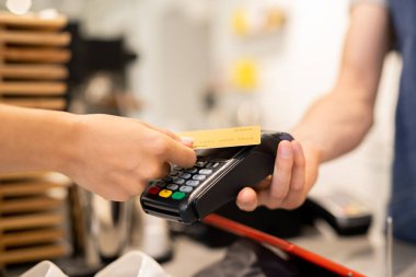 Kafenin genç müşterisi, garsonun ya da baristanın yiyecek ve içecek parasını öderken elinde tuttuğu elektronik ödeme makinesinin üzerinde plastik kart tutuyor.