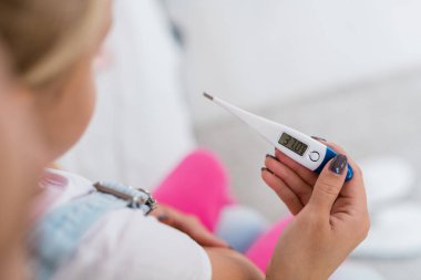 Hasta kızının sıcaklığını ölçtükten sonra termometreyi tutan genç annenin eli.