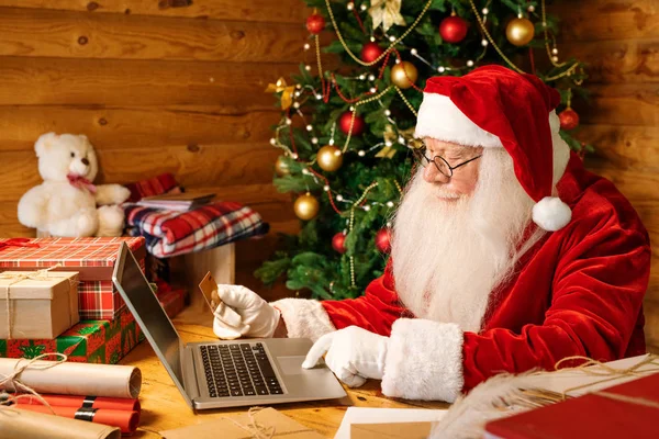 Hedendaagse Kerstman Kostuum Zitten Aan Balie Voorkant Van Laptop Terwijl — Stockfoto