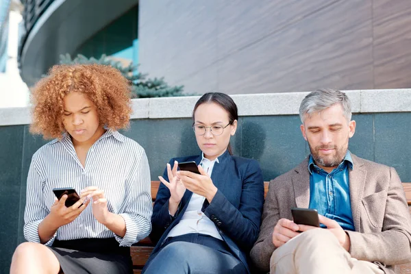 Row Young Mobile Employees Sitting Bench Wall Scrolling Smartphones Work — Stock Photo, Image