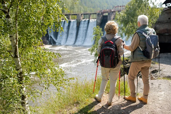 后视镜中 一对成熟的夫妇背着背包站在河岸上 在桥边的瀑布边掠过 — 图库照片