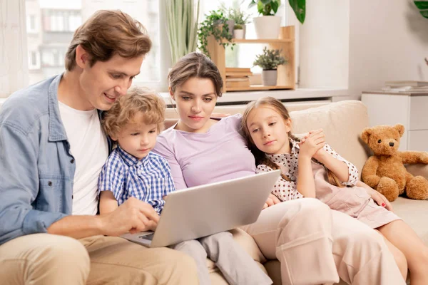 年轻而轻松的家庭 穿着便服在笔记本电脑上看电影 坐在沙发上挨家挨户 — 图库照片