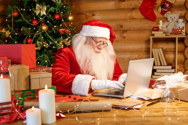 Papai Noel Sentado Mesa Madeira Frente Laptop Enquanto Olha Através — Fotografia de Stock