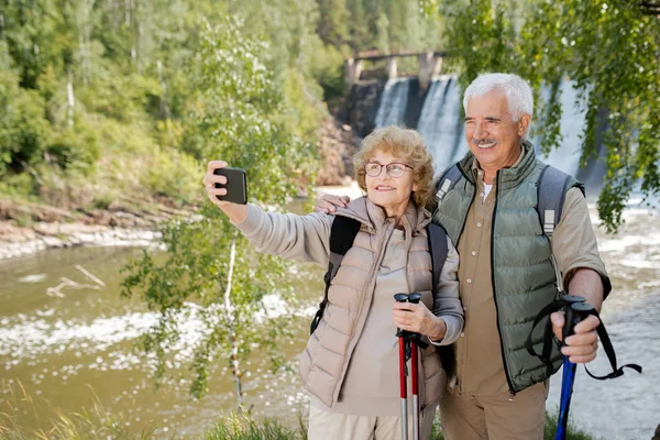 Uśmiechnięci Seniorzy Kijami Trekkingowymi Robią Selfie Podczas Swojej Podróży Naturalnym — Zdjęcie stockowe