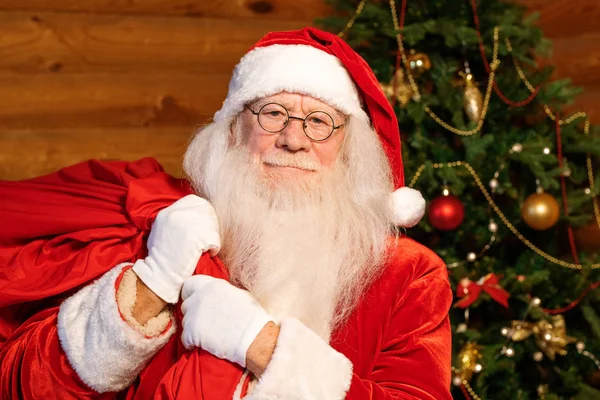 圣诞快乐圣诞老人 身穿传统服装 头戴白色手套 戴着眼镜 背着一大袋红包圣诞礼物送给孩子们 — 图库照片